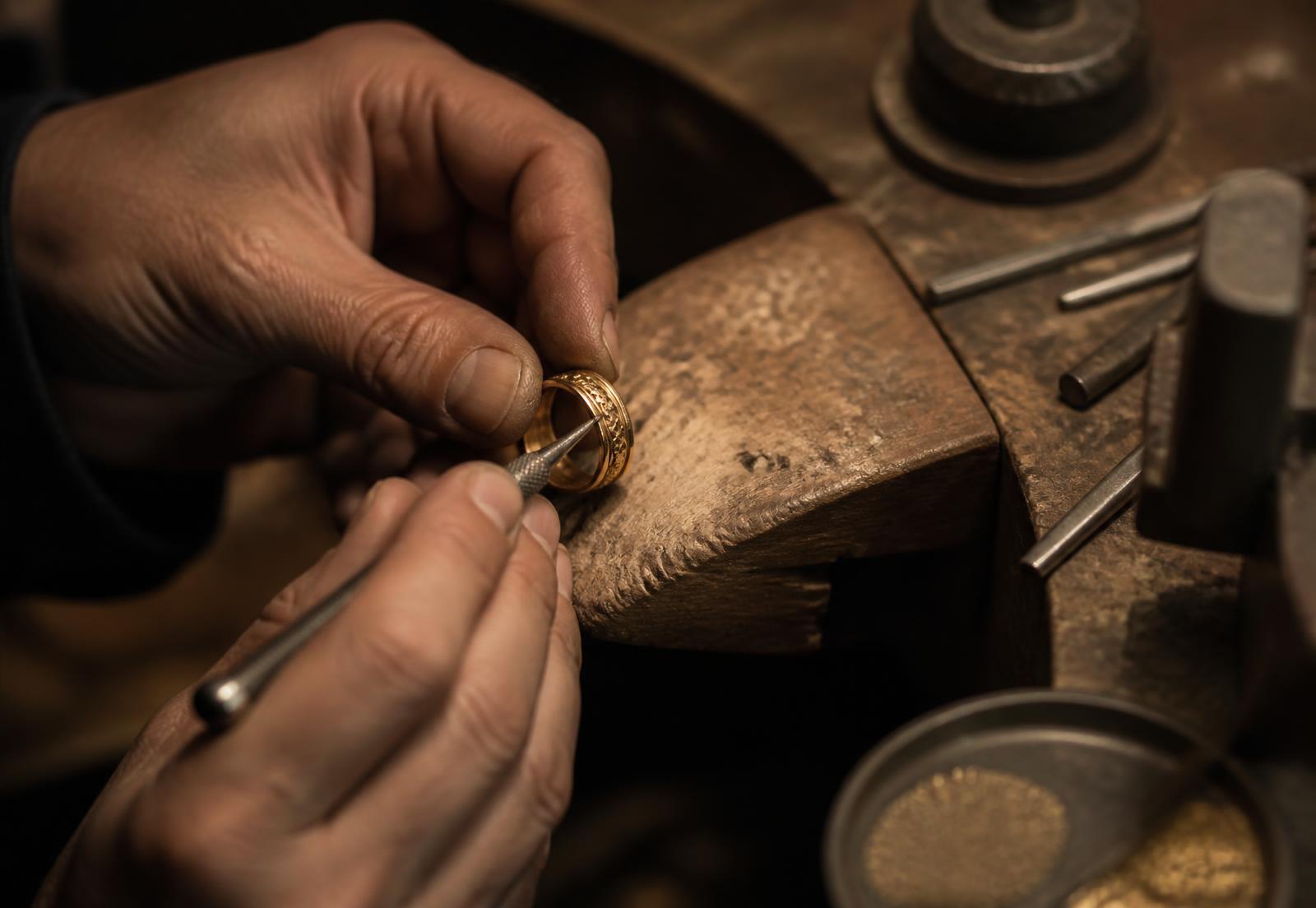 A goldsmith burnishing an engraved gold ring at a wooden bench